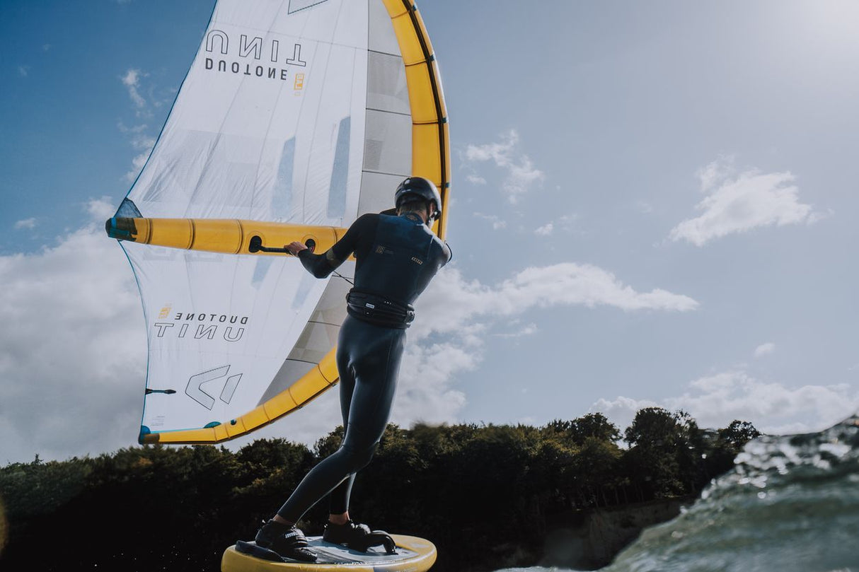 ION Mission 2026 Kite mit weißem Segel und gelben Streben, Kitesurfer in schwarzem Neoprenanzug auf dem Wasser in Aktion