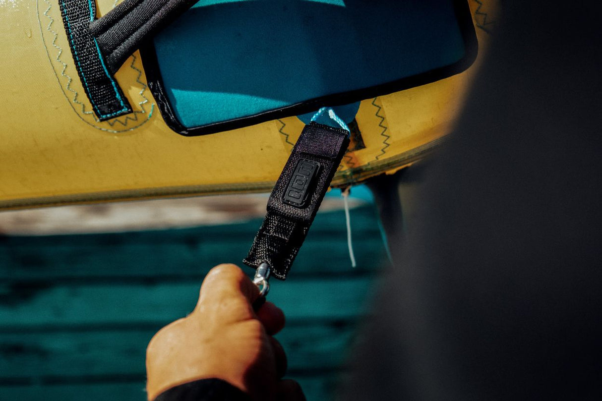 ION Wing Leash Core Dyneema Handgelenkschlaufe schwarz, befestigt an gelbem Kiteboard, Detail-Nahaufnahme