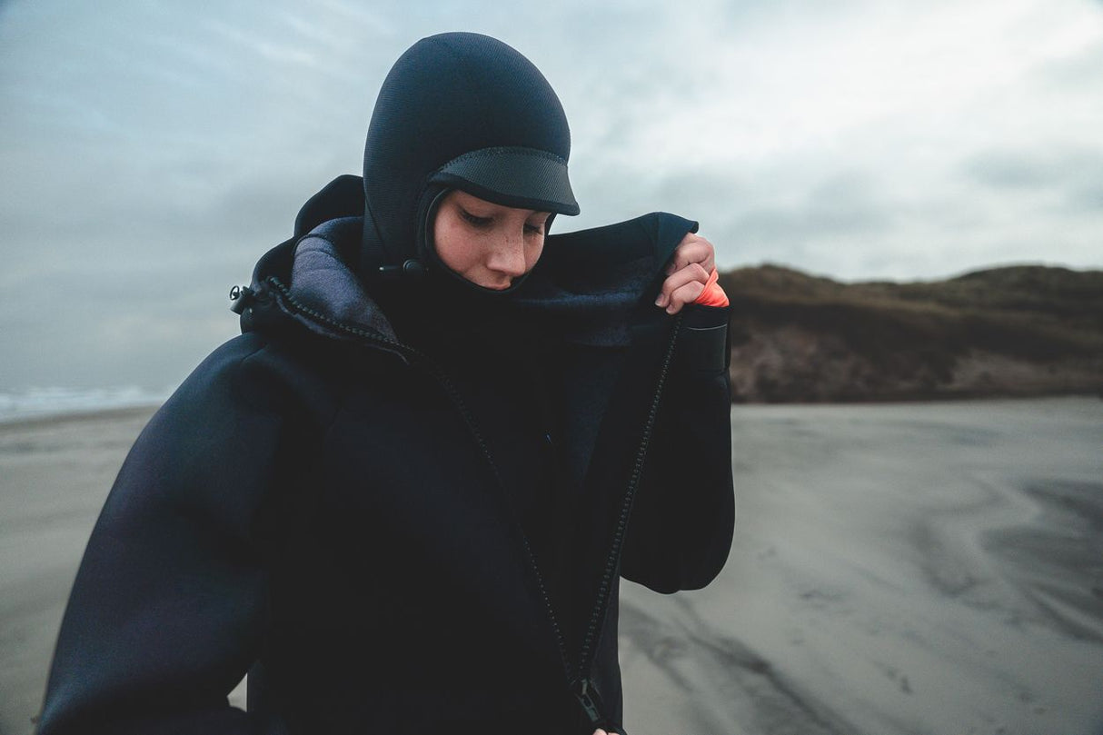 ION Neo Cosy Coat 2026 in Dunkelblau, Neopren-Jacke mit Kapuze, Frontalansicht am Strand getragen