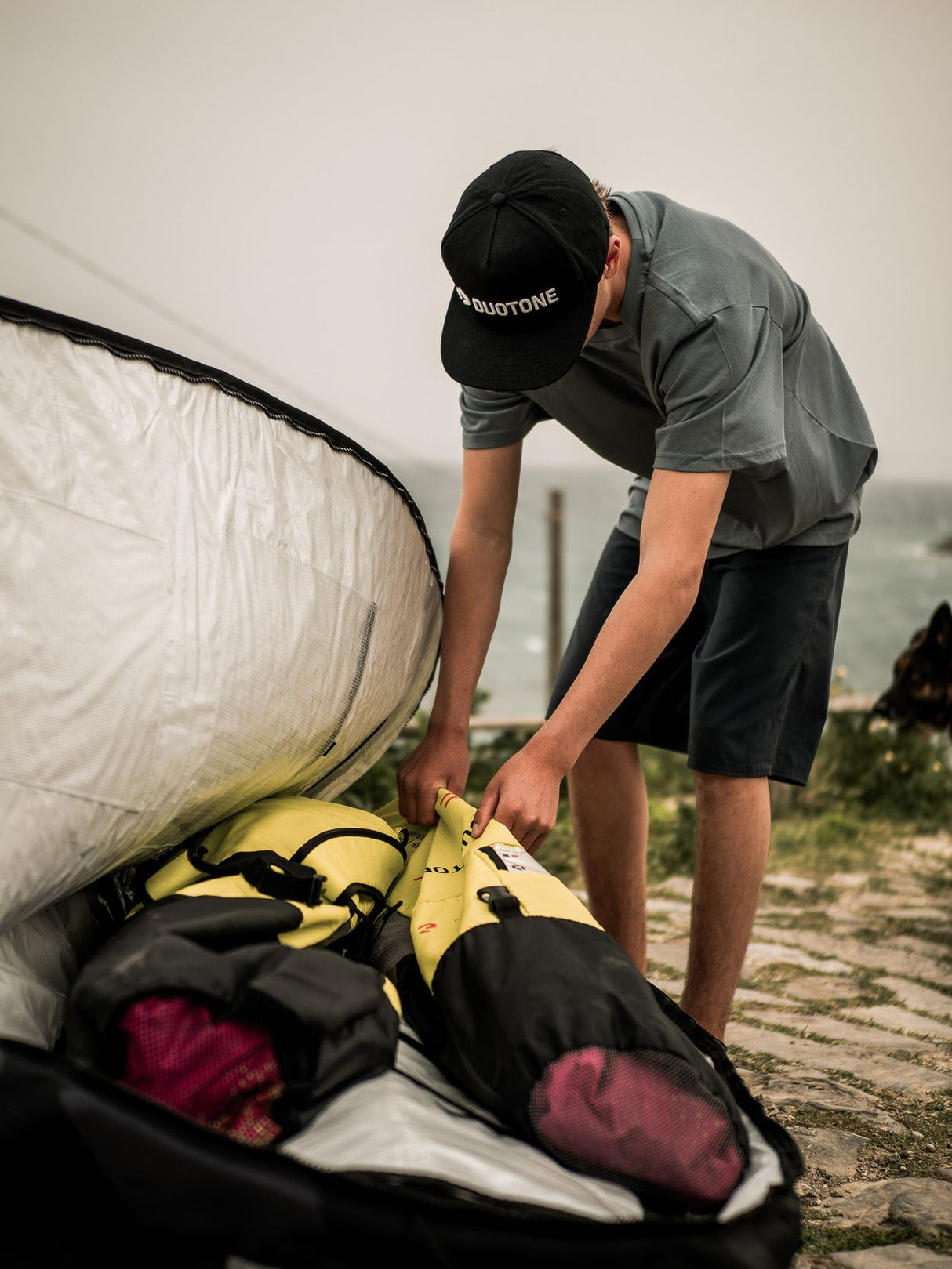ION Wing Boardbag Tec 2026 schwarz-weiß, Kitesegel-Transporttasche, Mann packt Tasche am Strand