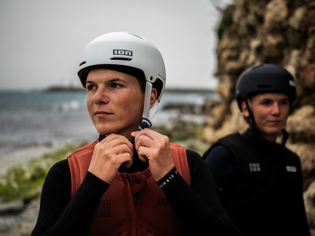 ION Slash Core Helm weiß, Sportschutzhelm mit Kinnriemen, Frontalansicht auf Person am Strand