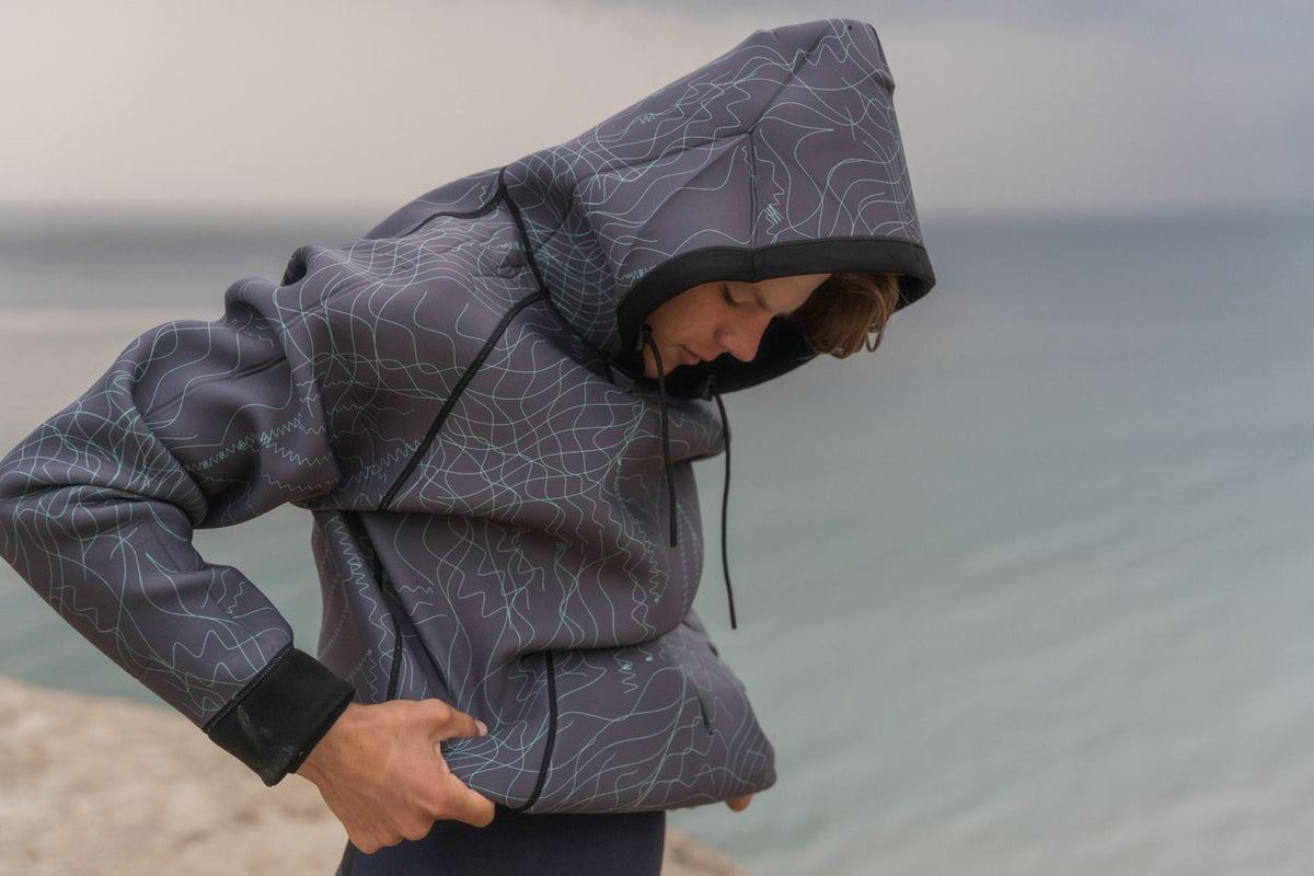ION Neo Hoody Reversible 2026, Neopren-Jacke mit Kapuze, Grau mit Muster, wasserabweisend, Frontalansicht am Strand getragen