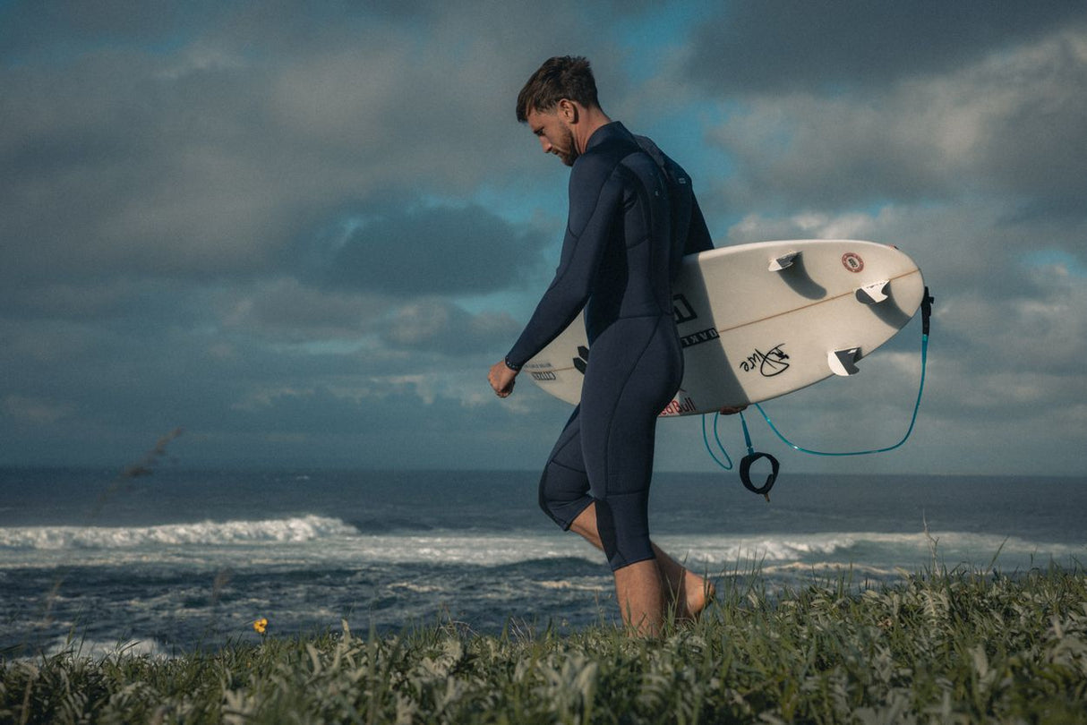 ION Element 4/3 Overknee LS Back Zip Neoprenanzug in Dunkelblau, Surfer trägt Anzug mit Surfbrett am Strand
