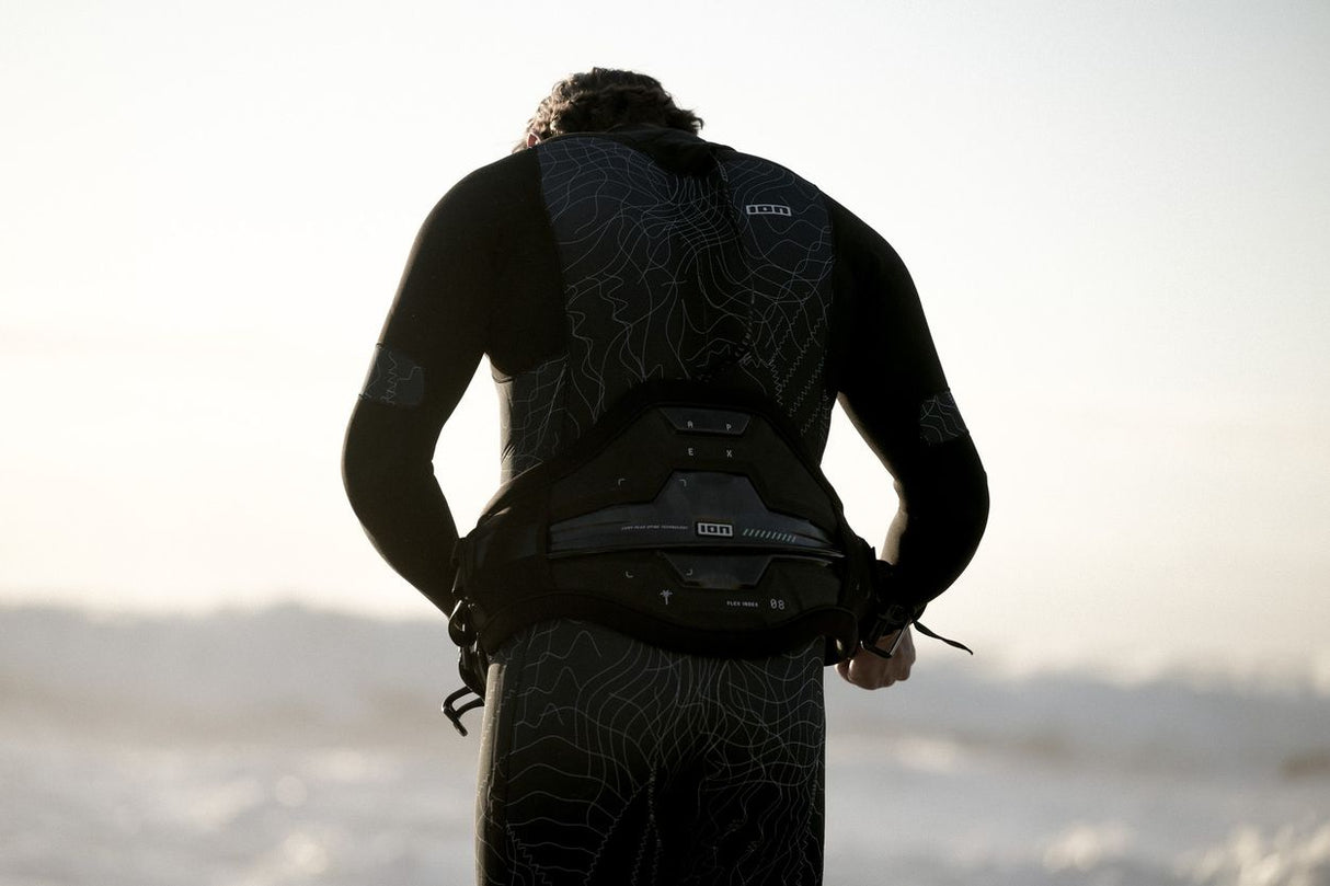 ION Apex Kite Trapez Herren 2026 in Schwarz, Frontalansicht mit Träger am Strand