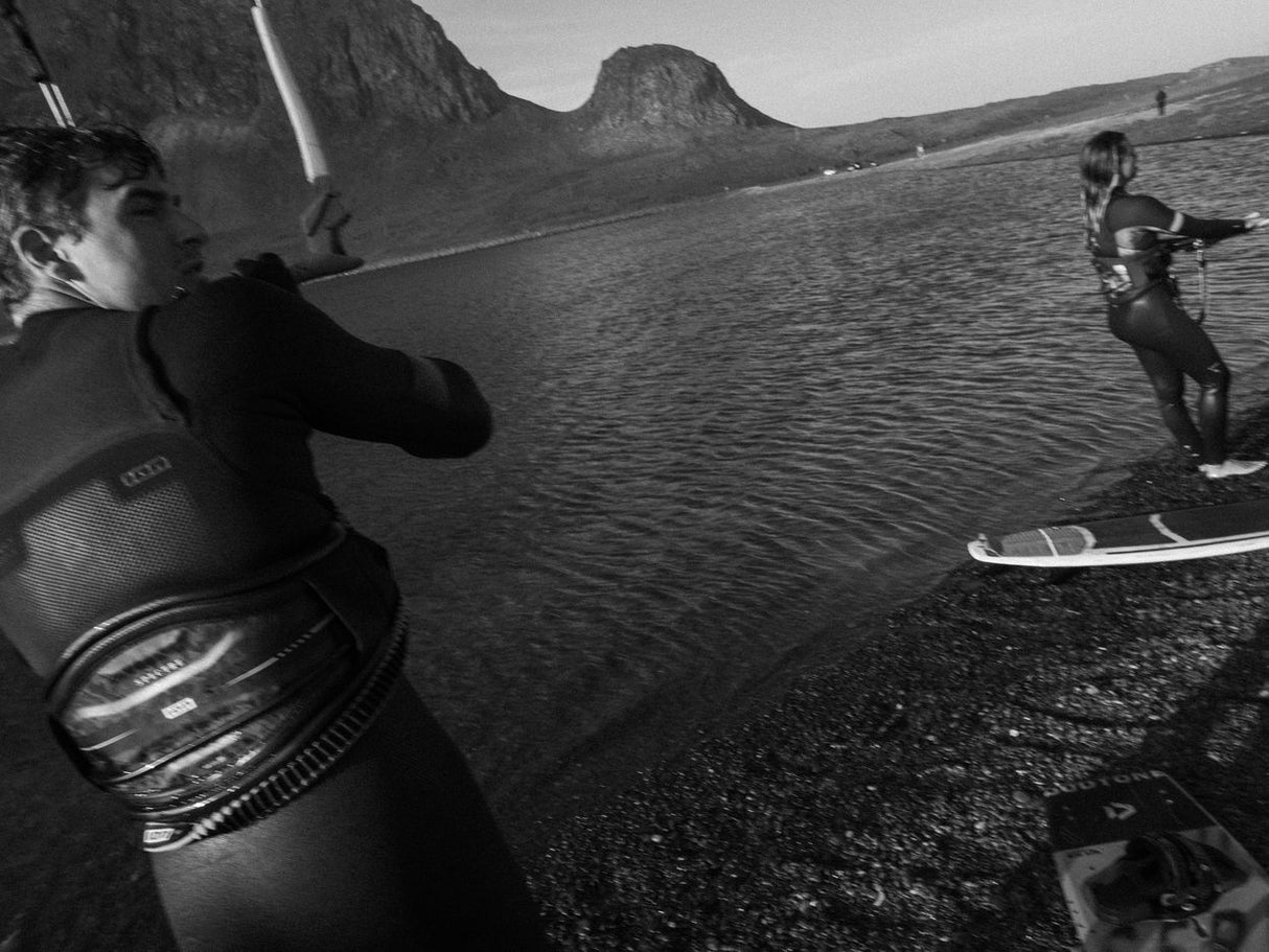 ION Spectre 2026 Kiteboard schwarz in Aktion beim Kitesurfing am Wasser, Seitenansicht