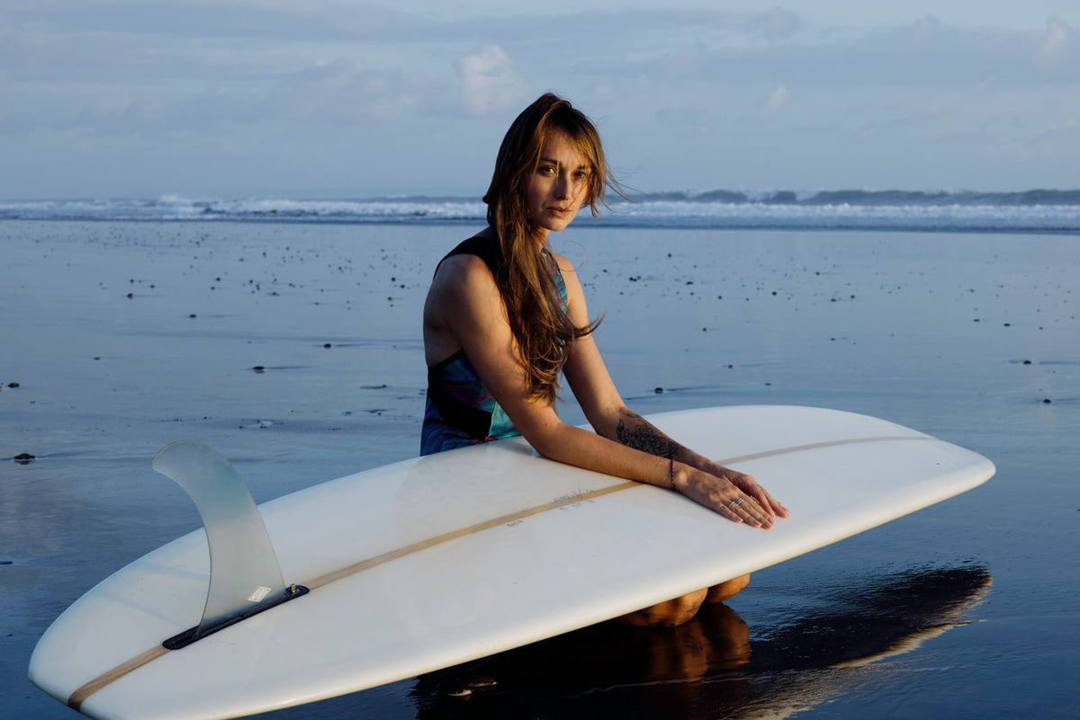 ION Amaze V-Back 1.5 Damen Neoprenanzug in Schwarz, Frontansicht mit Surfboard am Strand