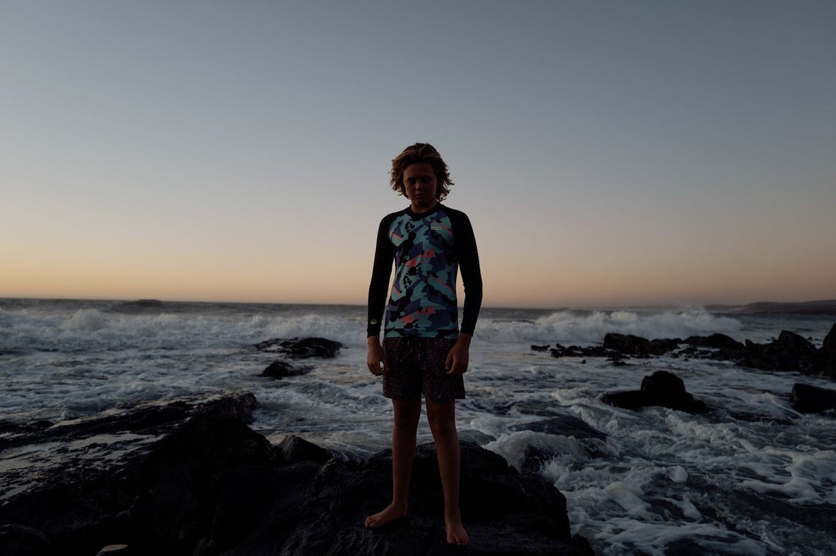 ION Capture Junior 2026 Neoprenanzug, Junge in schwarzem Wetsuit mit farbigem Muster am Strand