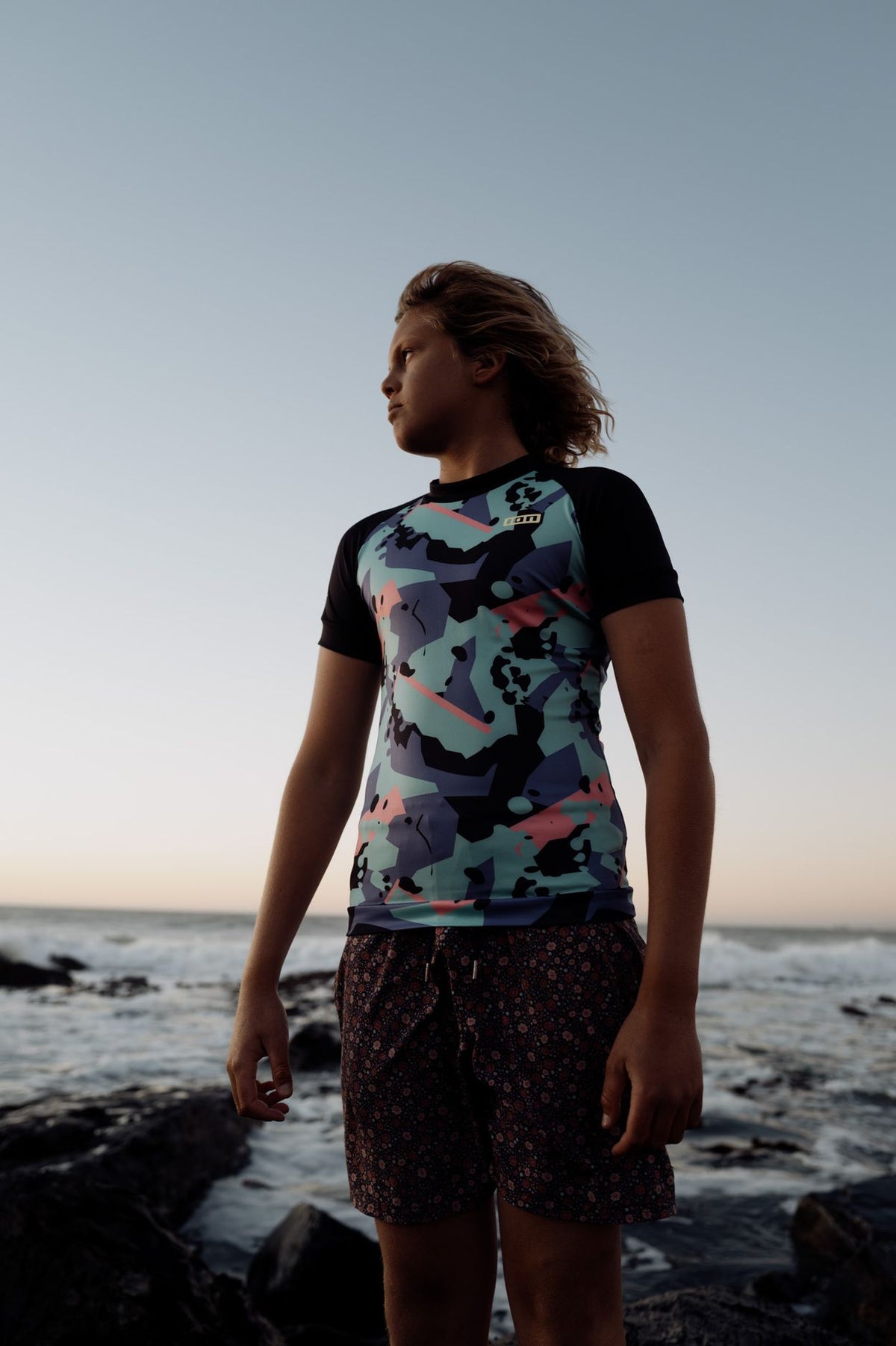 ION Rashguard Capture 2026, schwarzes Shirt mit buntem Muster, Frontansicht am Strand getragen