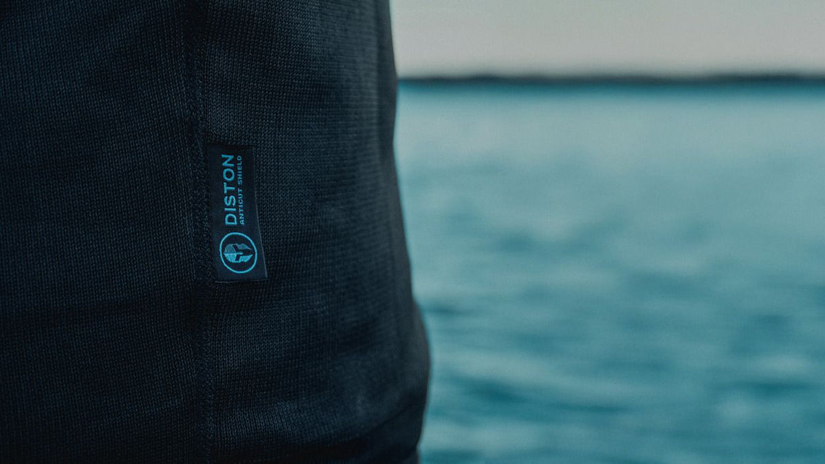 ION Rashguard LS Surf Shield SS2026, dunkelblau, Langarm-Neopren Oberteil, Detail mit Logo, Nahaufnahme vor Meer