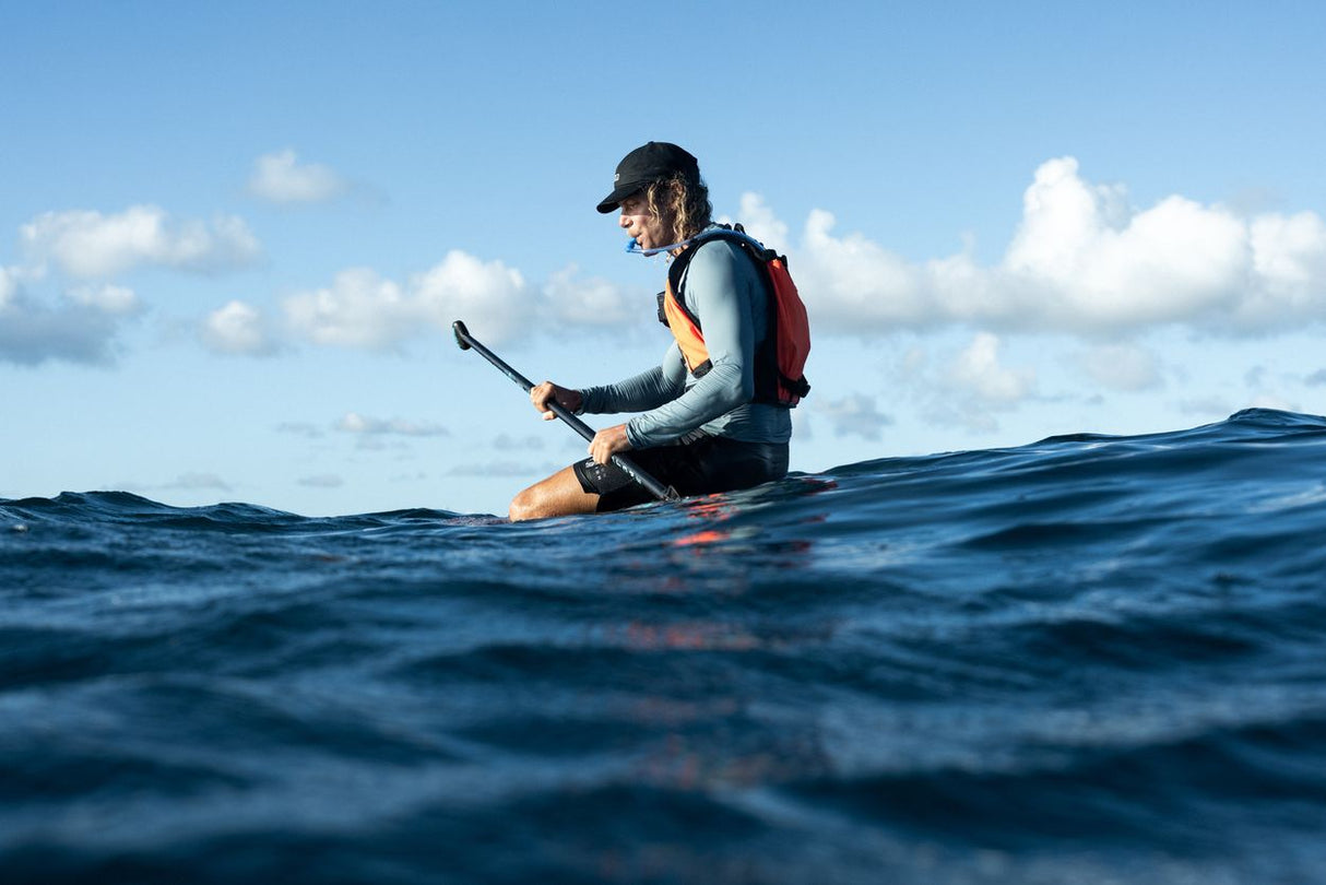ION Explorer Bag 2026 rot-blau, Wassersportler auf Board mit Rucksack, Seitenansicht im Wasser