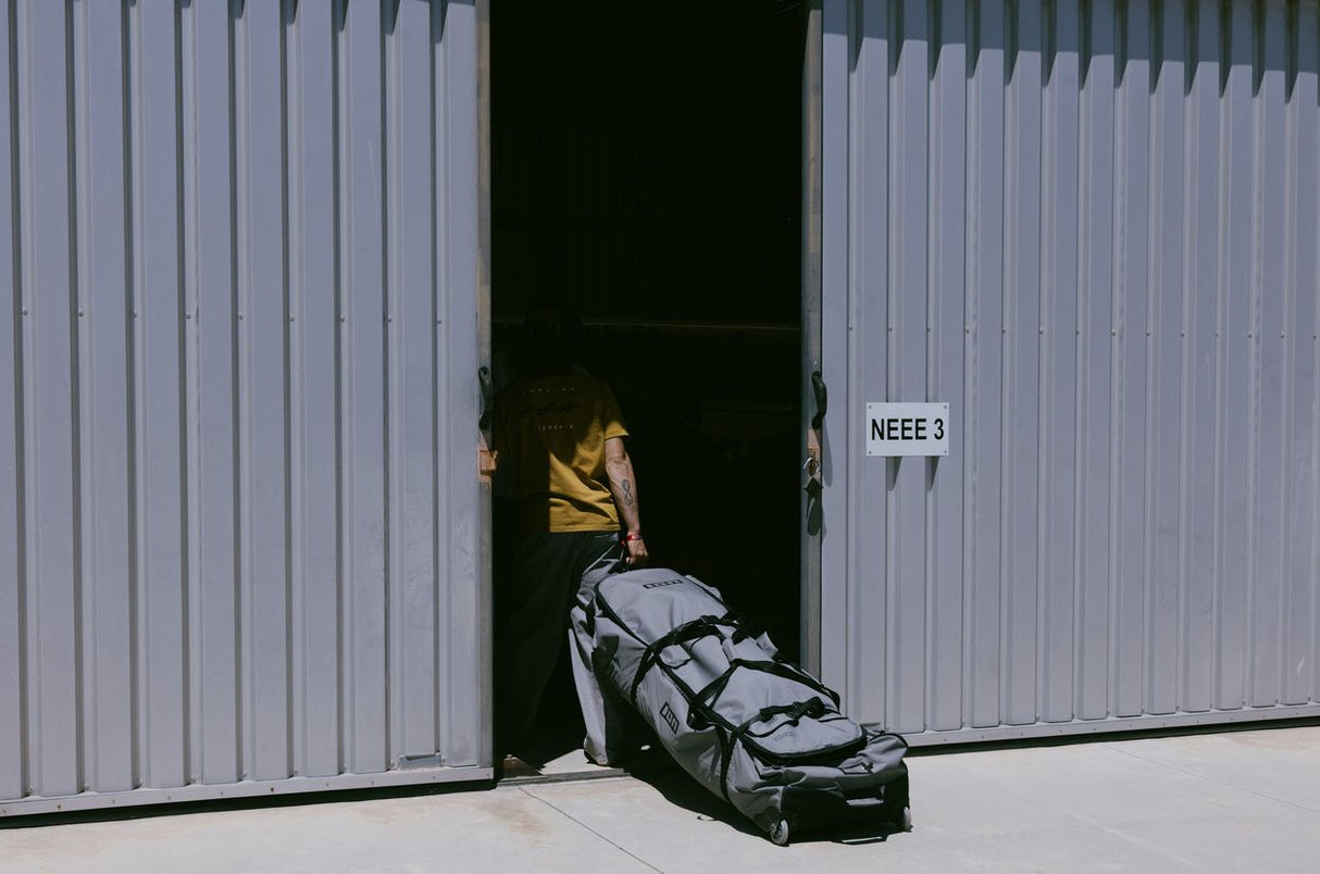 ION Kite Gearbag Core 2026, grau-schwarze Tasche mit Rollen, vor offener Hallentür, Frontalansicht