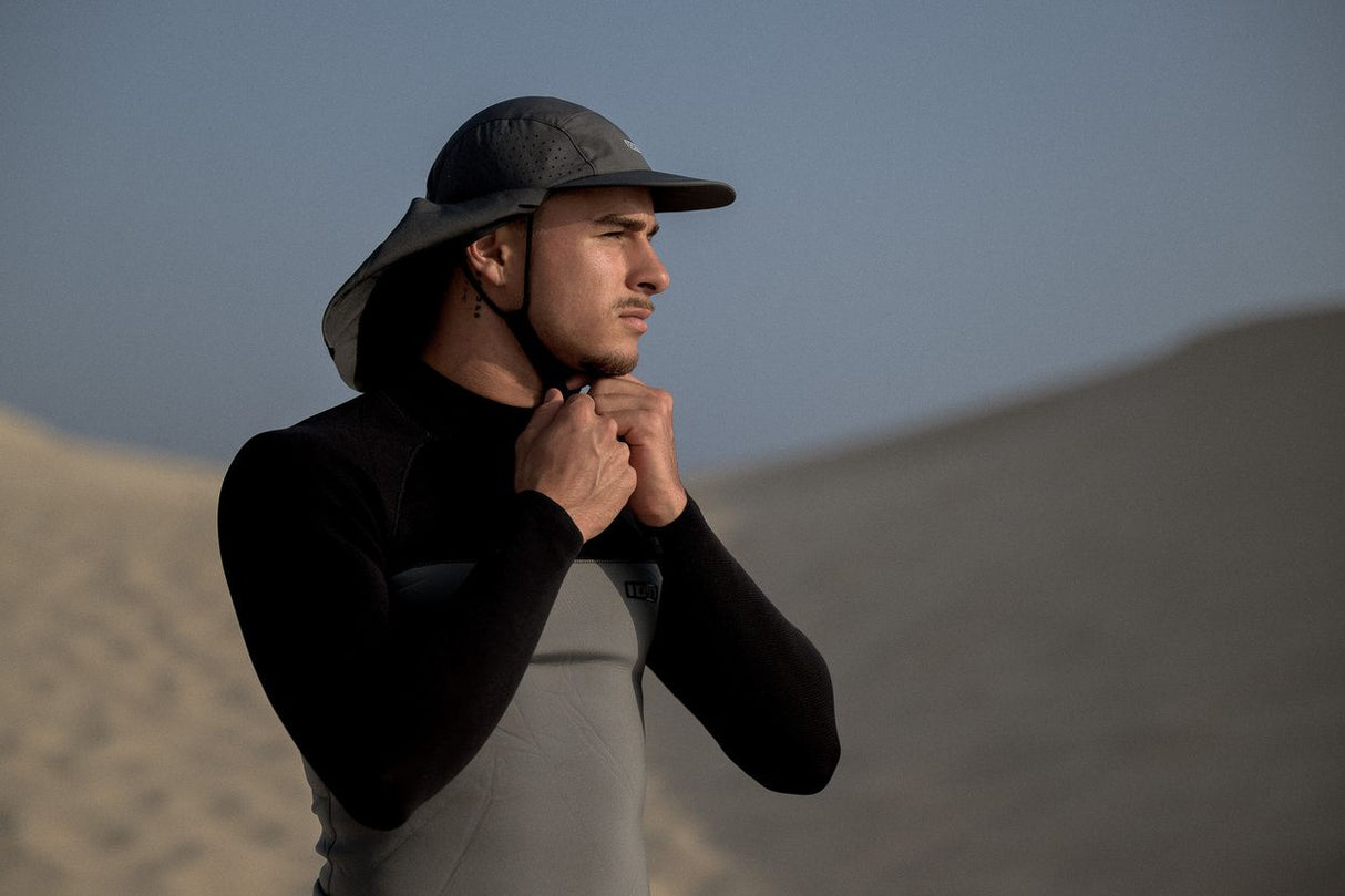 ION Surf Cap Pro 2026 schwarze Kappe mit Nackenschutz, seitliche Ansicht am Strand getragen