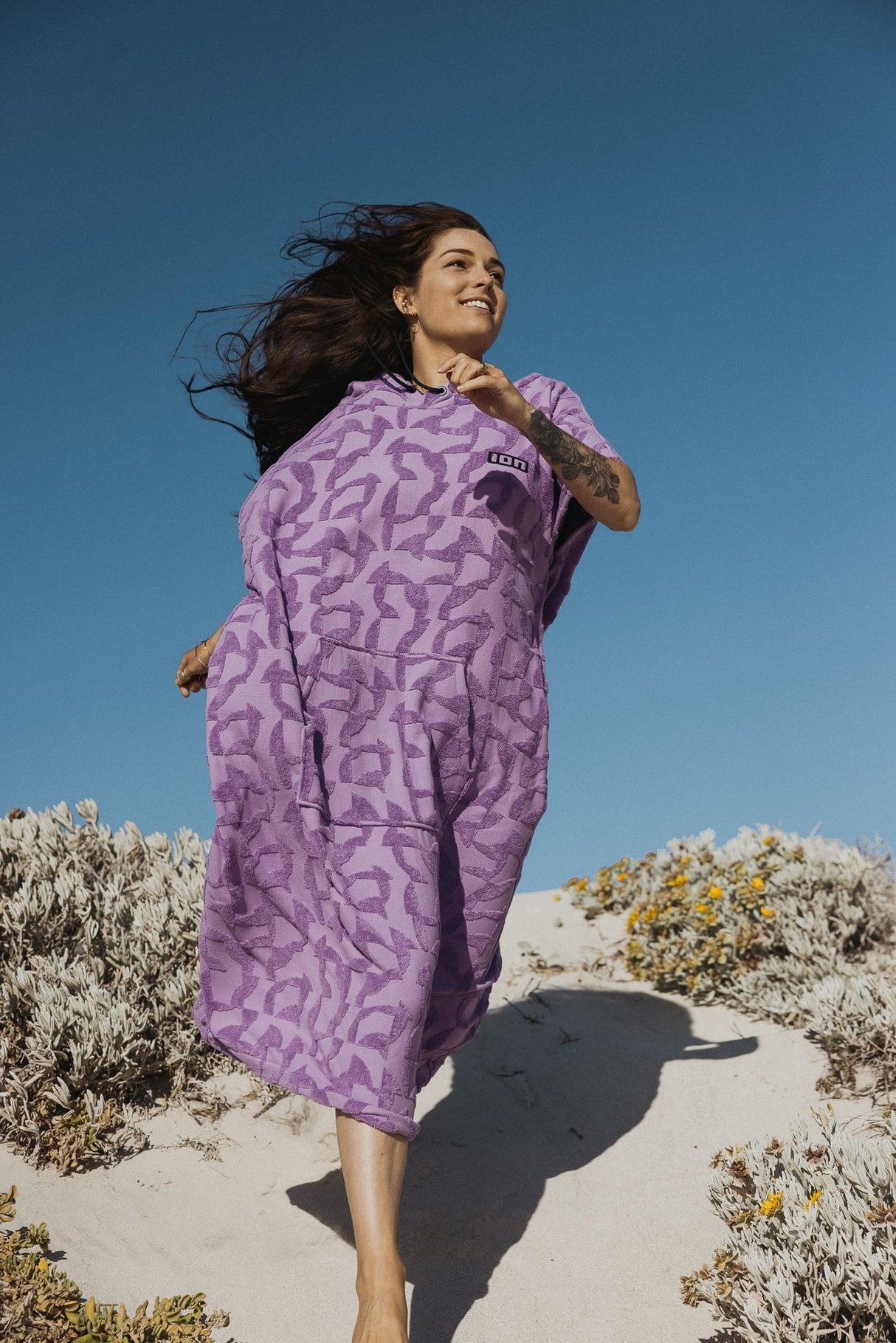 ION Surf Poncho Select Reefside 2024 in Violett mit geometrischem Muster, getragen am Strand