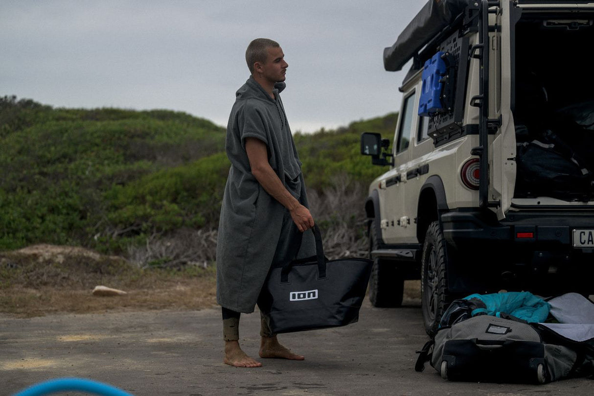 ION Surf Poncho Element 2026 grau, Wechselrobe aus Baumwollmischung, Mann trägt Poncho am Strand neben Campervan