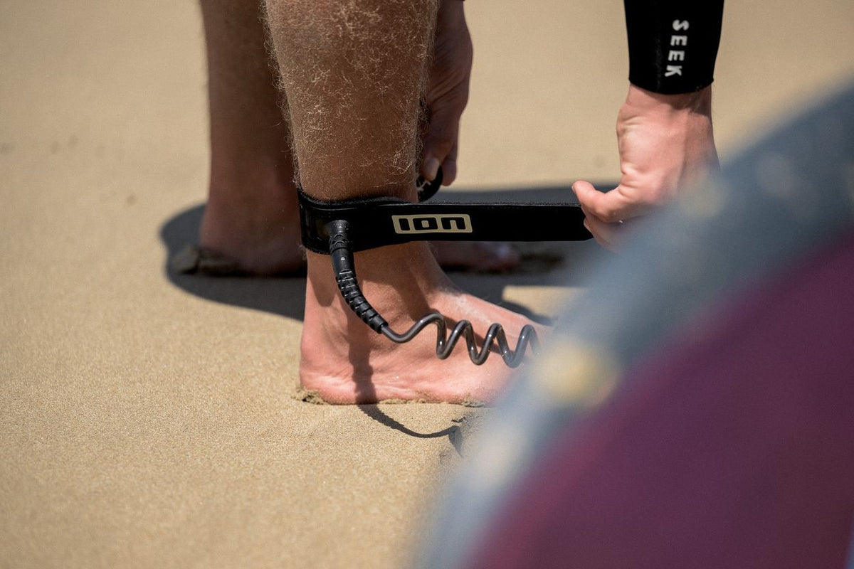 ION Wing Board Leash Core Coiled Ankle schwarz, Spiralkabel, am Fuß getragen am Strand