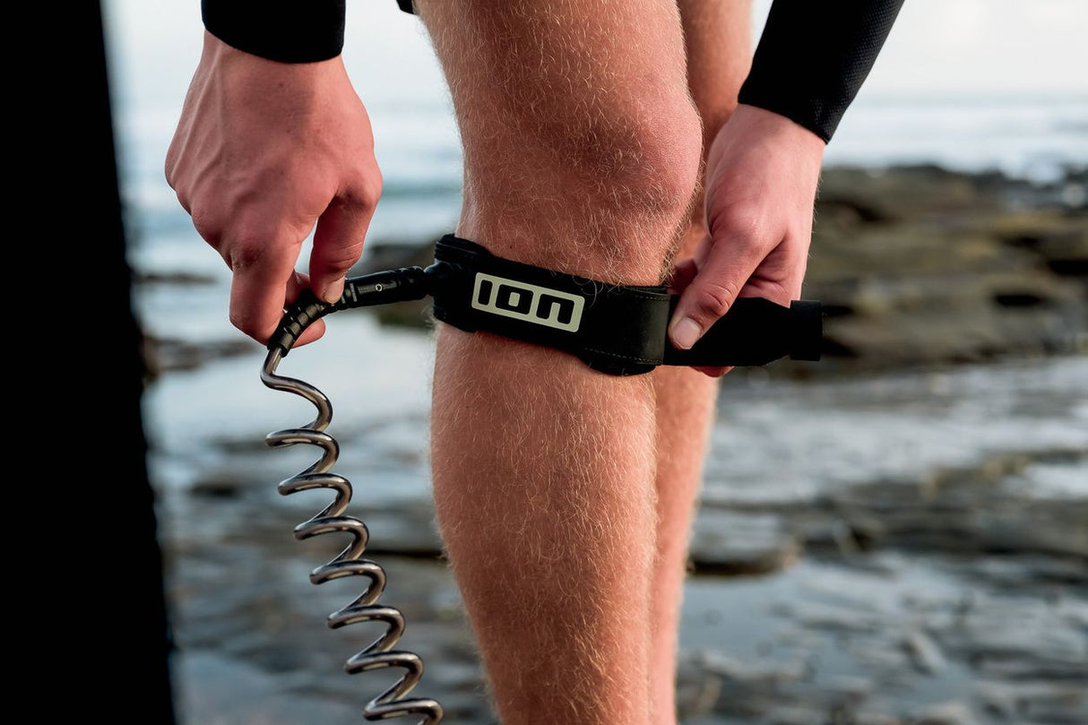 ION Wing Board Leash Core Coiled Knee, schwarzes Neopren-Fußband mit spiralförmiger Verbindungsleine, Nahaufnahme am Bein