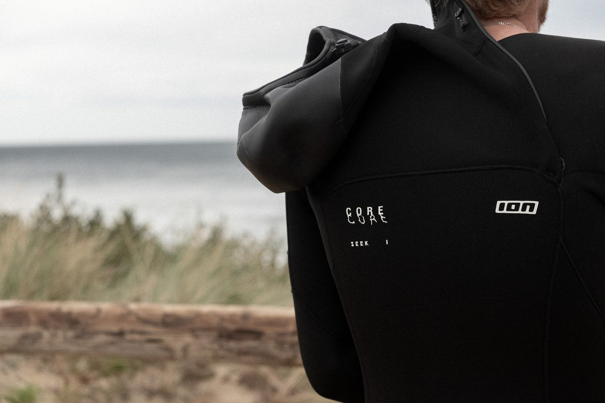 ION Seek Core 5/4 Hood Front Zip Neoprenanzug in Schwarz mit Kapuze, Rückansicht am Strand