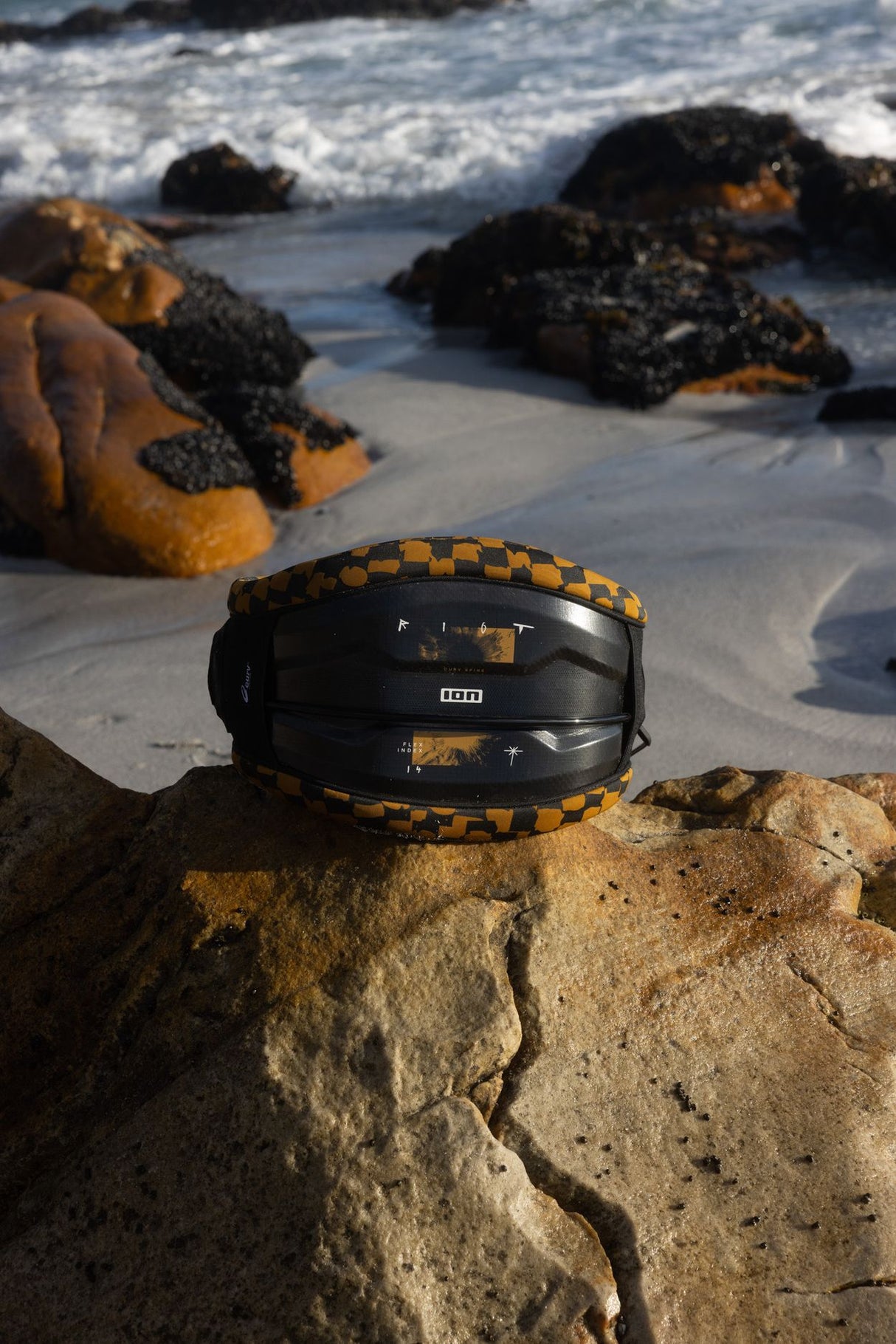 ION Riot Curv 2026 Kite-Waist in Schwarz mit goldenem Rand, am Strand positioniert
