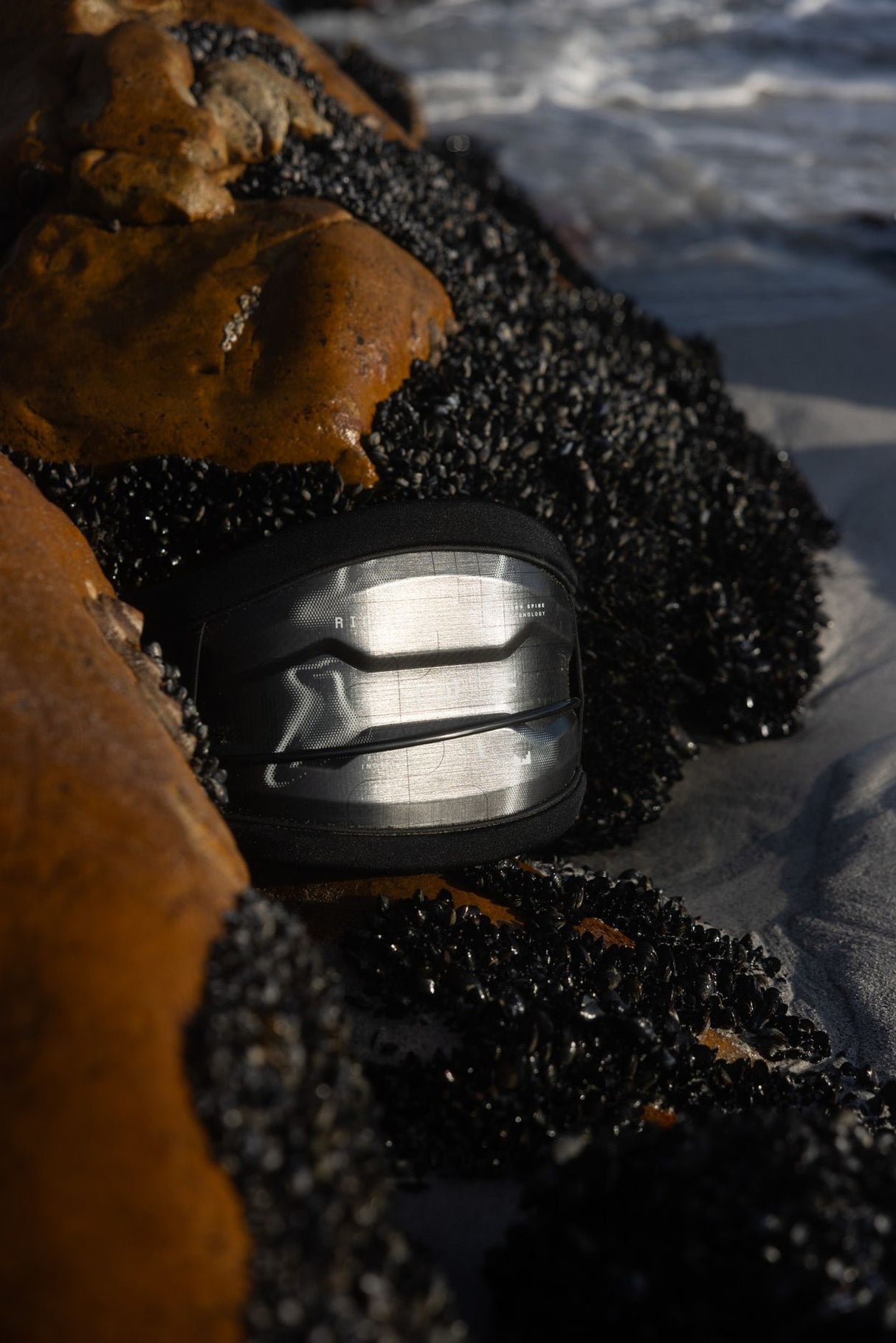 ION Riot Curv 2026 Kiteboard mit schwarzem Obermaterial und Grifffläche, Detail-Nahaufnahme der Bindung am Wasser