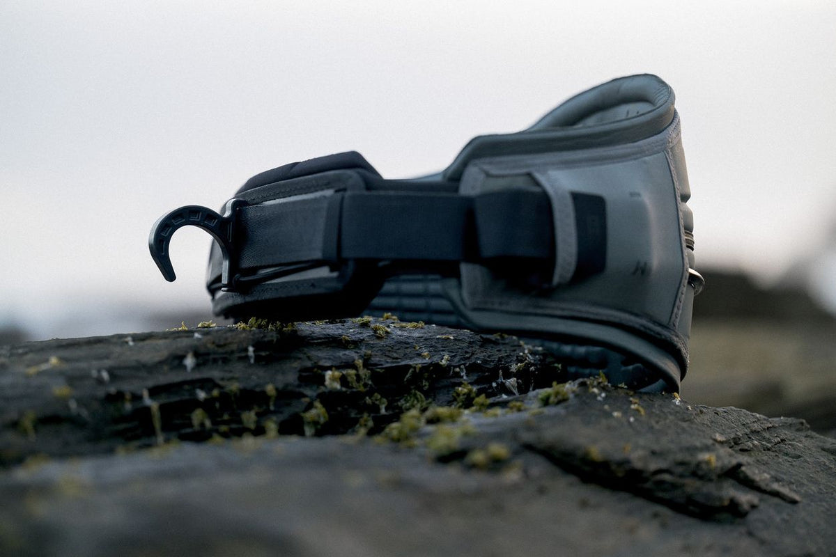 ION Rave 2026 Kiteboarding Trapez in Schwarz, Seitenansicht auf Stein, robustes Design mit Verschlüssen