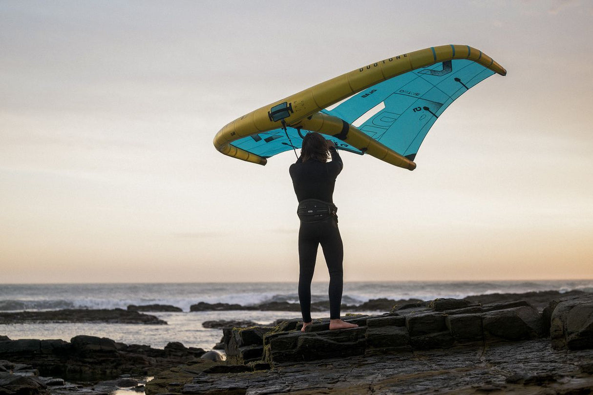 ION Rave 2026 Kite in Blau-Olive, von vorne gehalten, am Strand mit Meer im Hintergrund