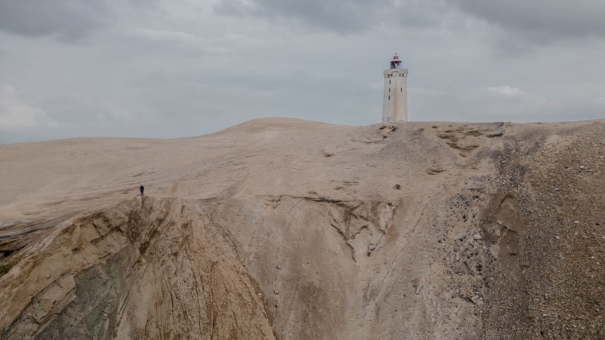 ION Neo Bommel Beanie 2026 Strickmütze in Grau, Frontansicht auf sandiger Dünenlandschaft mit Leuchtturm