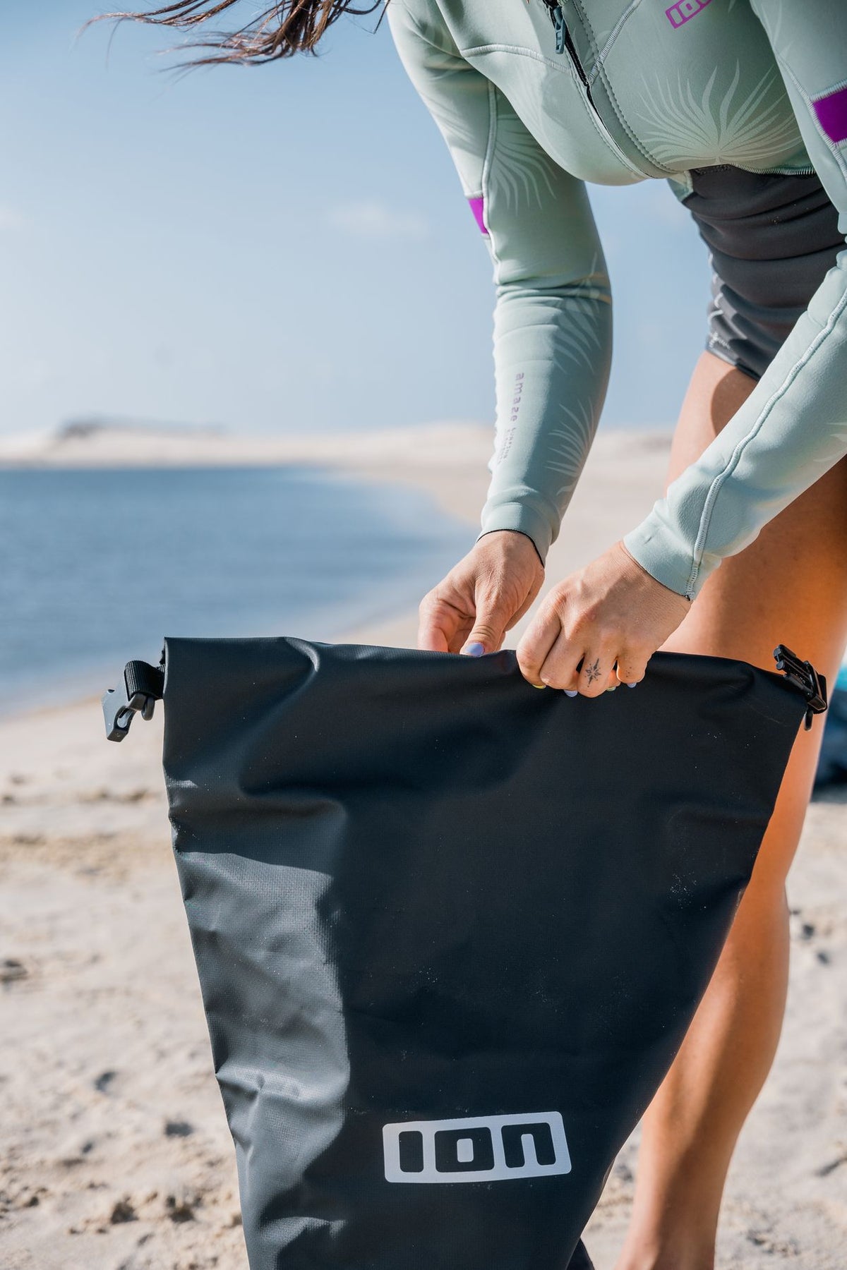 ION Dry Bag 2026 schwarz, wasserdichte Tasche mit Rollverschluss, am Strand in Händen gehalten