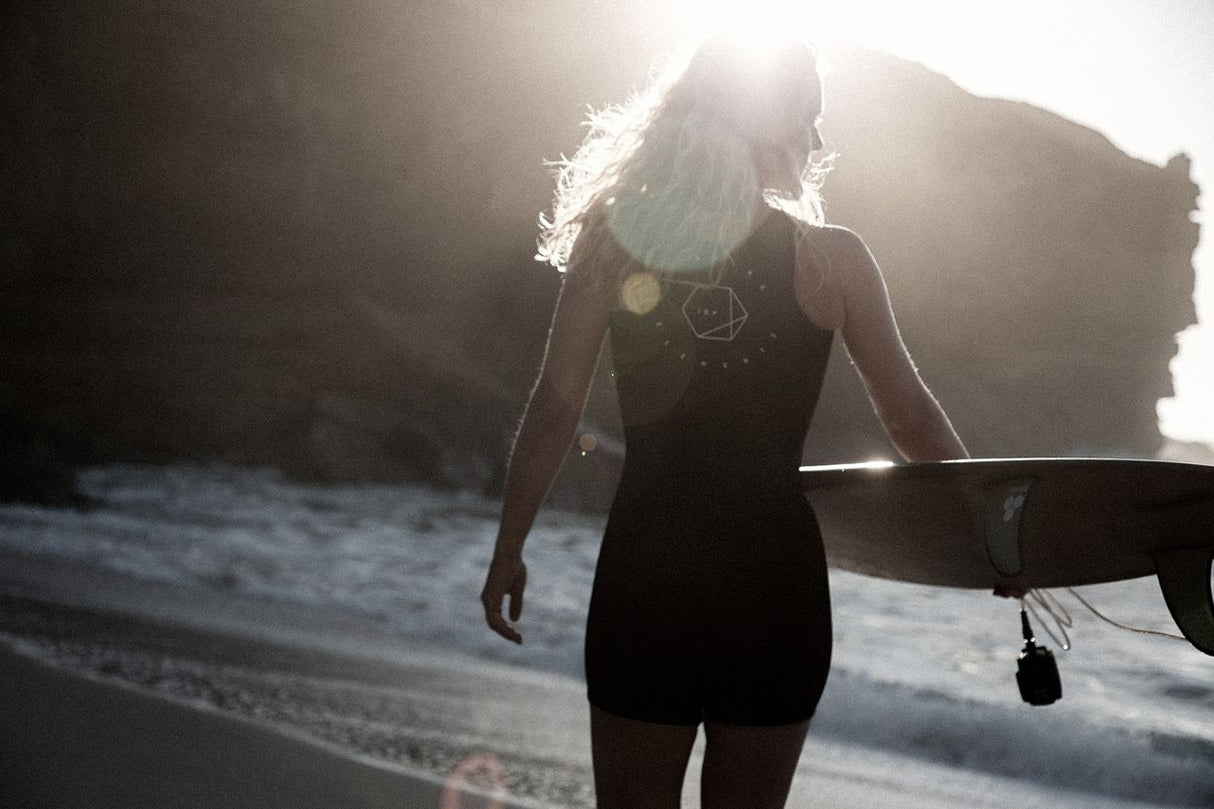 ION Monoshorty 0.5 Damen Neoprenanzug schwarz, Frau mit Surfbrett am Strand