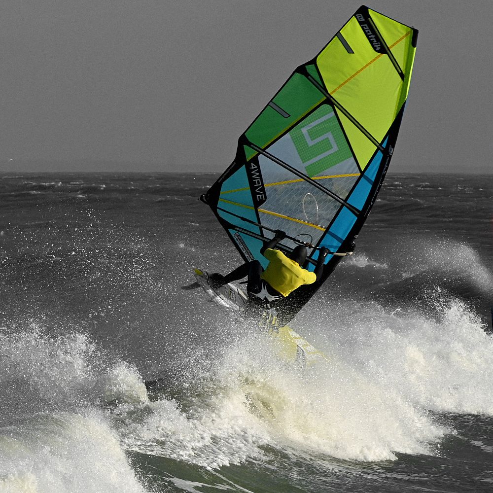 Patrik 4-Wave Windsurfboard mit neongelb-grünem und blauem Segel in Aktion auf dem Wasser