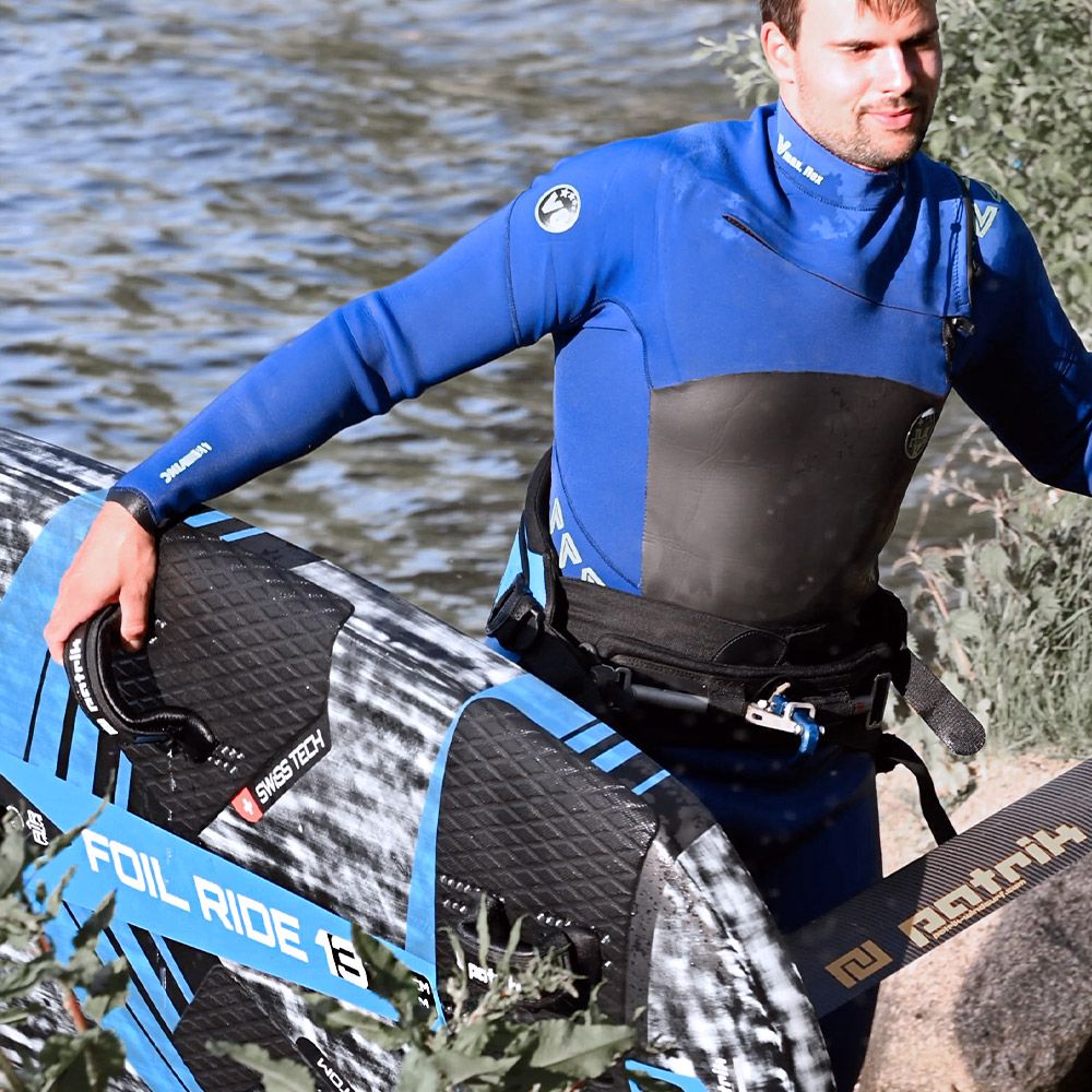 Patrik Foil Ride Kiteboard in Blau-Schwarz, Athlet mit Neoprenanzug am Wasser haltend