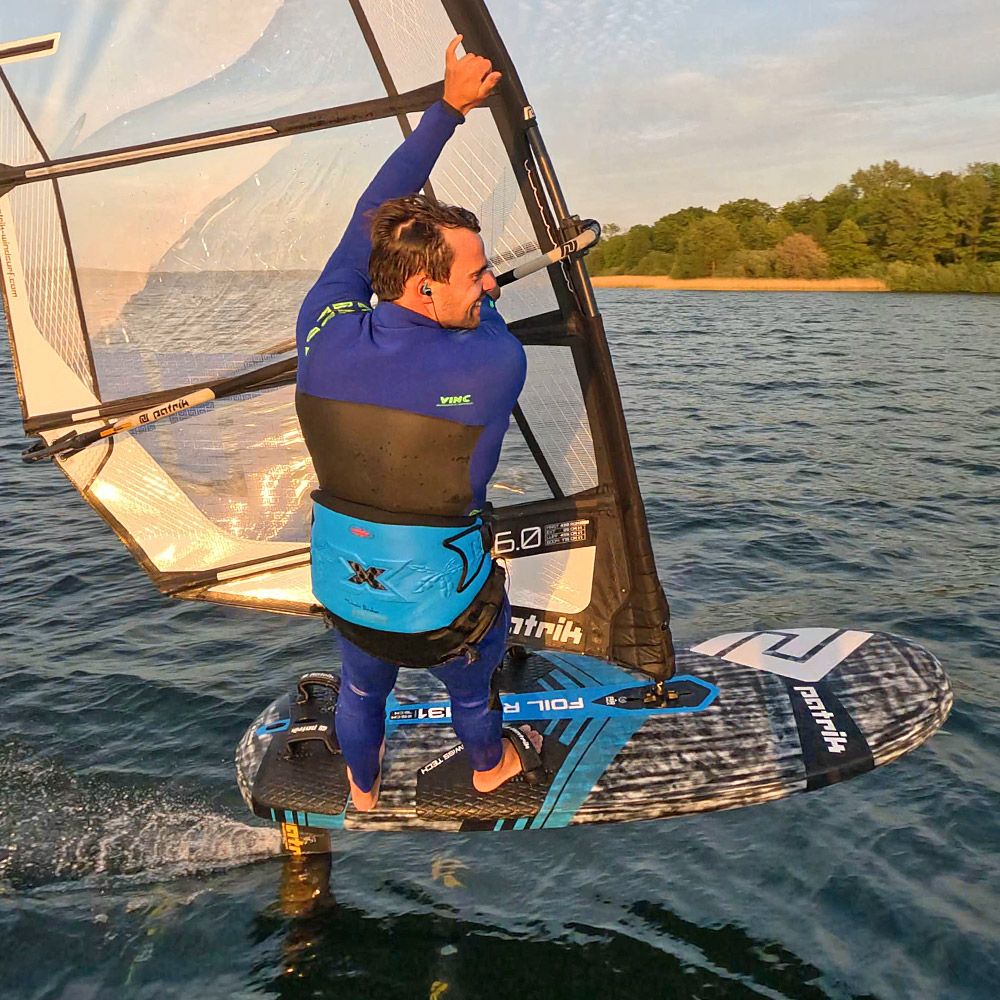 Patrik Foil Ride Foilboard mit Segel, blau-schwarzes Design, Foiler in Action auf dem Wasser