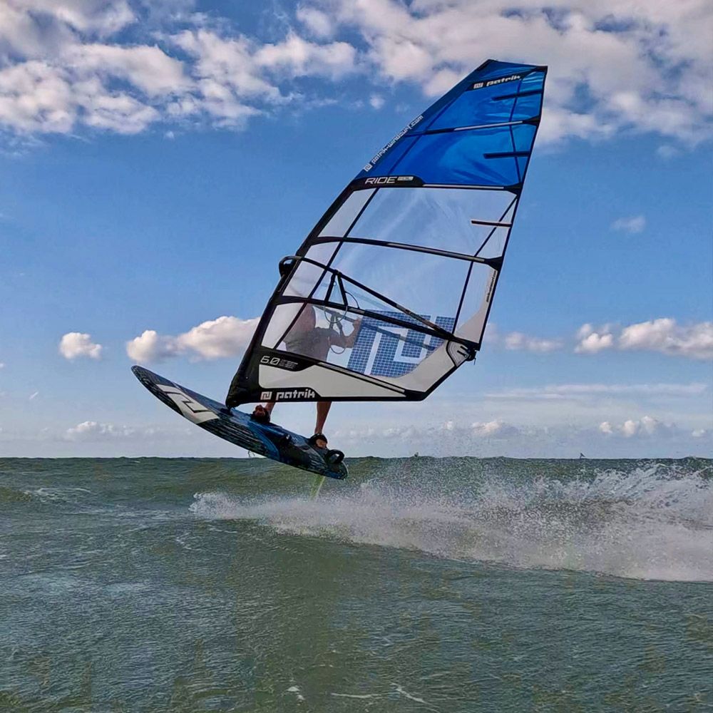 Patrik Ride Foil Windsurfboard blau schwarz in Aktion auf dem Wasser mit Welle und Himmel