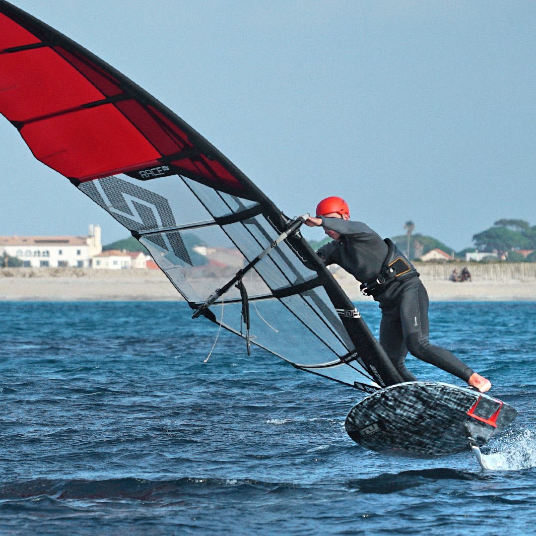 Patrik Foil Slalom Gen3 Windsurfboard rot-schwarz in Aktion auf dem Wasser mit Segler