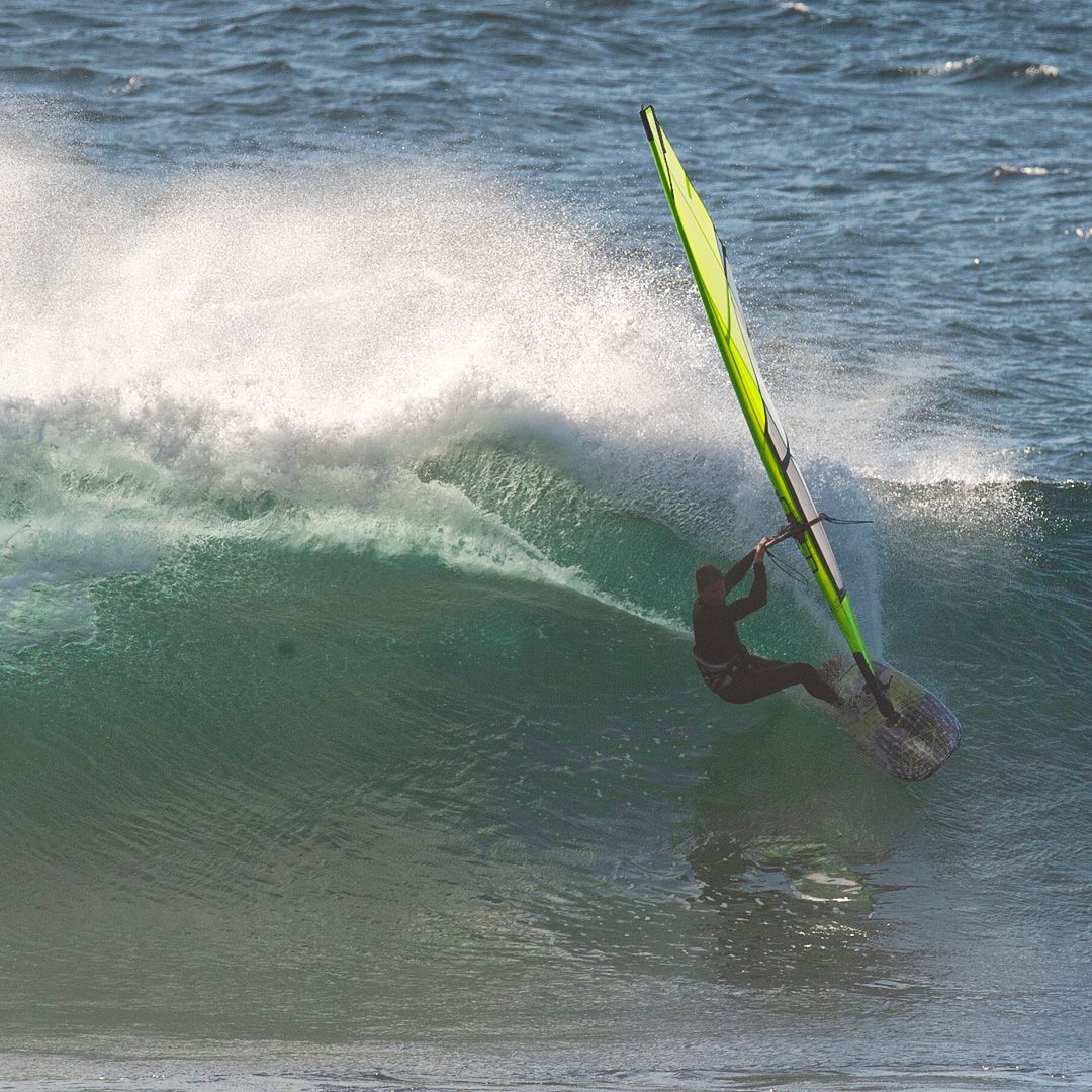 Patrik F-Wave Windsurfboard mit neongelben Segel in Aktion auf Welle, Seitenansicht