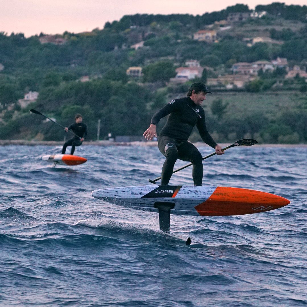Chase DW-X Downwind SUP in Blau-Orange, Athlet beim Fahren auf Wasser mit Paddel, Flügel sichtbar