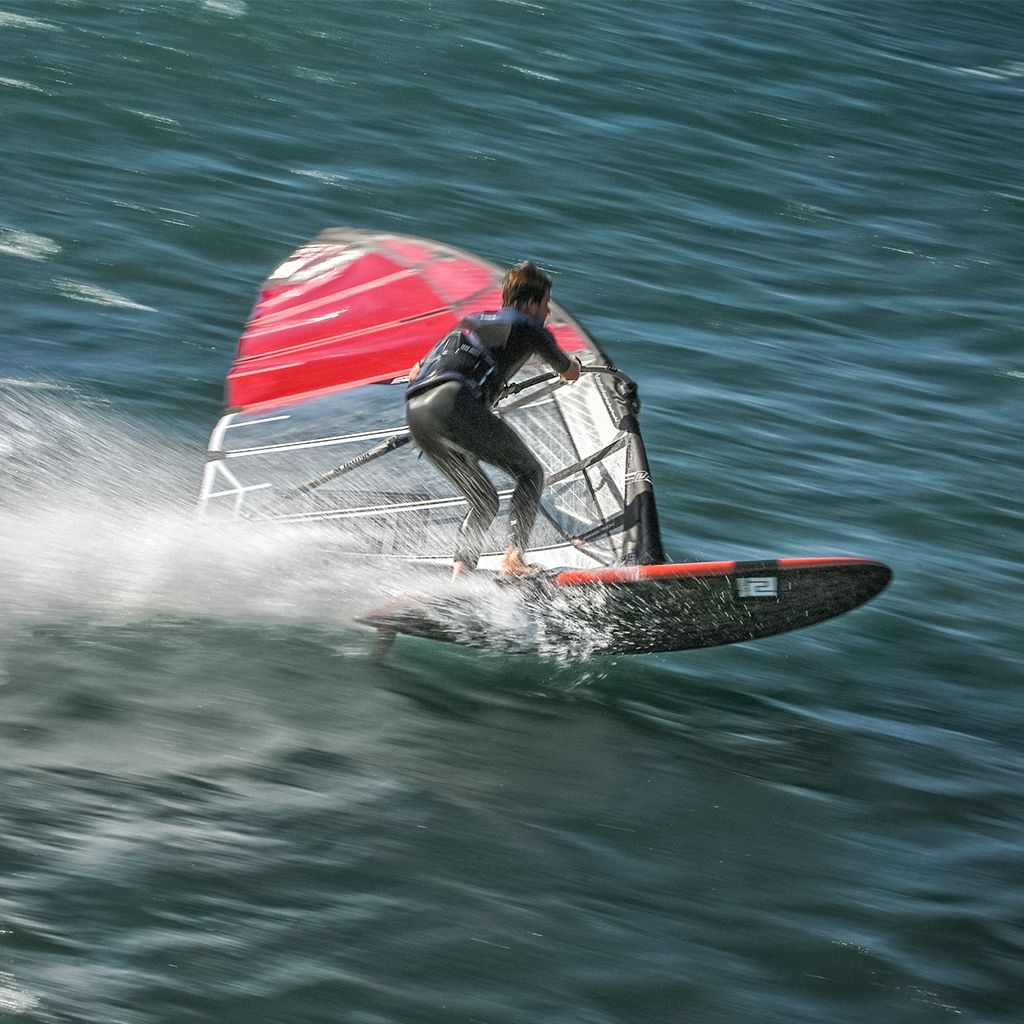 Patrik Slalom Windsurfboard in Aktion auf dem Wasser mit rotem Segel und Fahrer in Bewegung