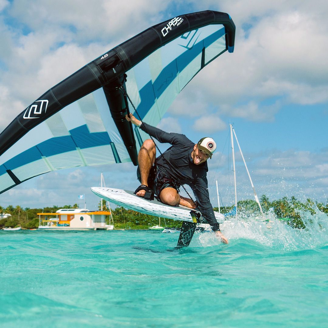 Chase WB-X Foilboard in Blau-Weiß, Athlet beim Foilen über türkisem Wasser mit schwarzem Kite