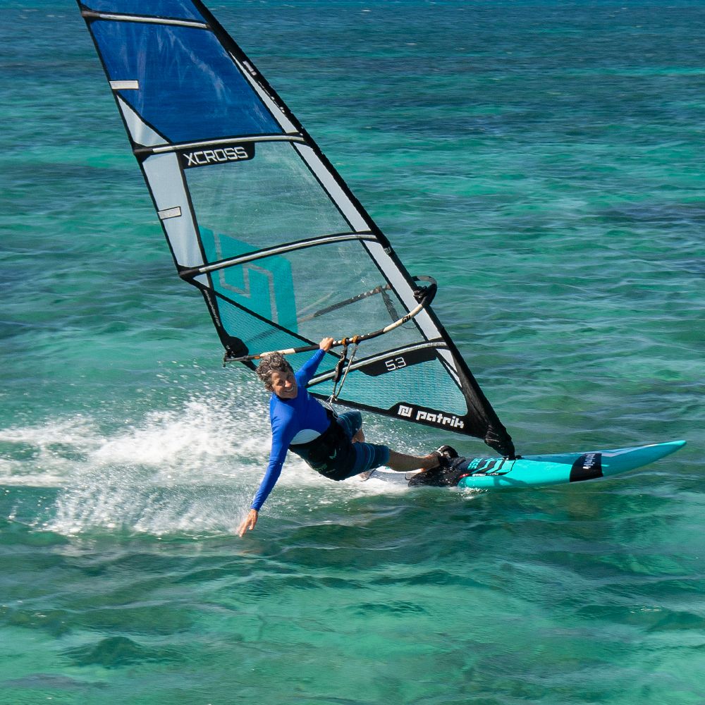 Patrik X-Cross Windsurfboard blau-weiß mit Segel im Wasser, Frontansicht beim Windsurfen