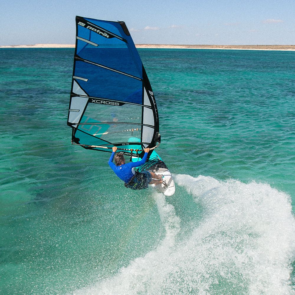 Patrik X-Cross Windsurfboard blau in Aktion auf türkisem Meer mit Wellen, Frontalansicht