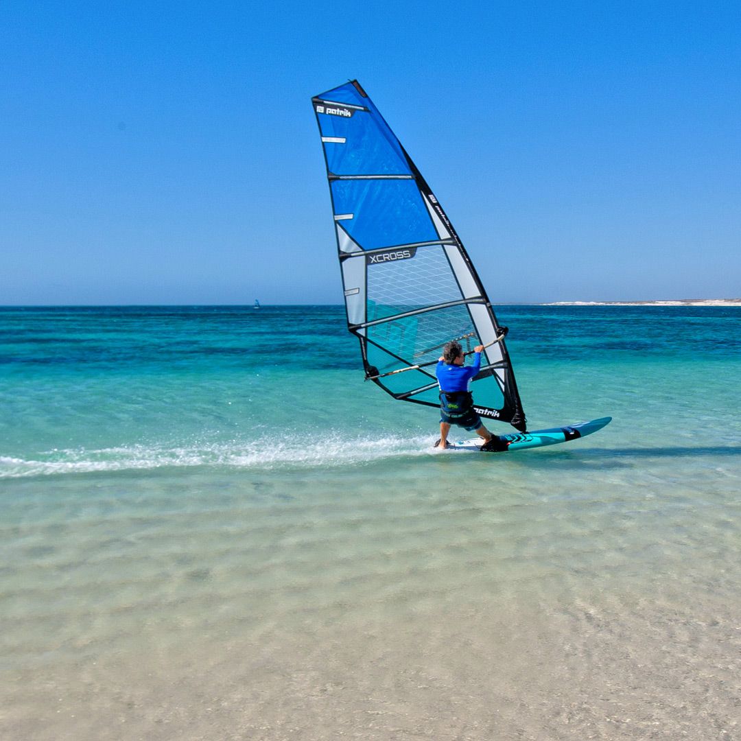 Patrik X-Cross X-Ply Windsurfboard blau mit schwarzem Mast im Wasser, Frontalansicht beim Windsurfen