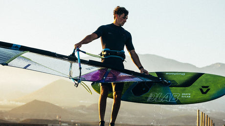 Duotone Skate D/LAB Kiteboard in Grün und Schwarz, Fahrer trägt Board unter dem Arm am Strand