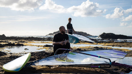 Duotone Super_Hero D/LAB 2027 Kiteboard in Blau und Weiß, am Strand mit Kitesurfern, Frontalansicht