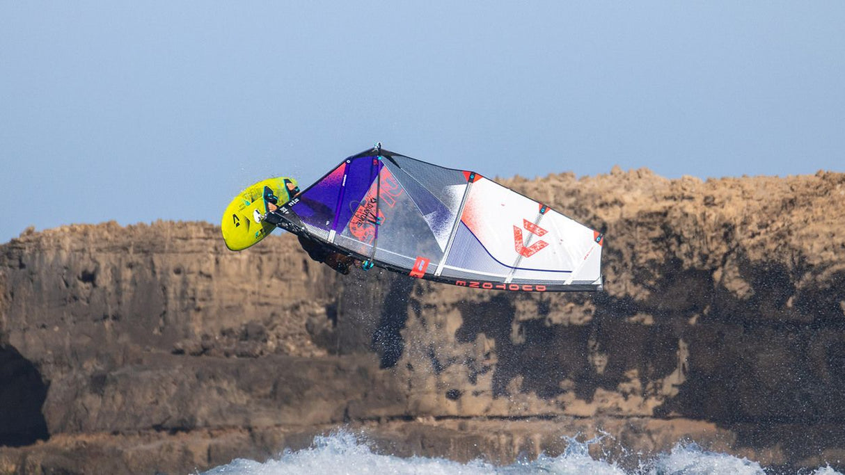 Duotone Super_Hero D/LAB 2027 Kitesegel in Blau, Weiß und Rot mit gelbem Kite-Bar, in Aktion über Wasser und Klippen