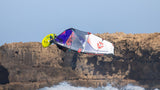 Duotone Super_Hero D/LAB 2027 Kitesegel in Blau, Weiß und Rot mit gelbem Kite-Bar, in Aktion über Wasser und Klippen
