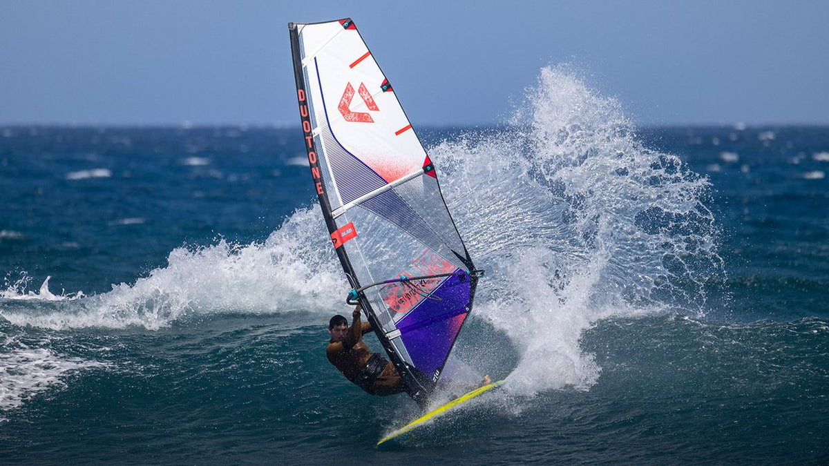 Duotone Super_Hero D/LAB 2027 Windsurfboard mit Segel in Weiß, Blau und Rot, Fahransicht auf Wellen
