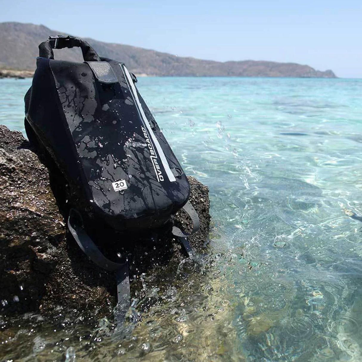 OverBoard wasserdichter Rucksack 30L schwarz, am Strand im Wasser, Frontansicht mit sichtbarem Reißverschluss