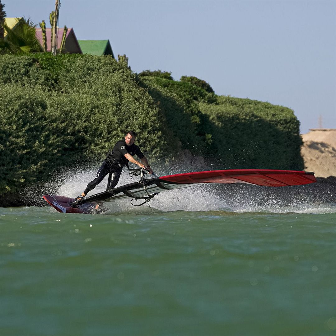 Patrik Slalom-X Windsurfboard rot-schwarz mit Segel in Action auf dem Wasser, Fahrer in Kurve