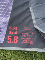 Duotone Duke SLS 5.8 Kite 2026, grau mit rot-violettem Duotone-Design, Detailansicht des Segels mit technischen Spezifikationen und Markenlogos auf Gras liegend