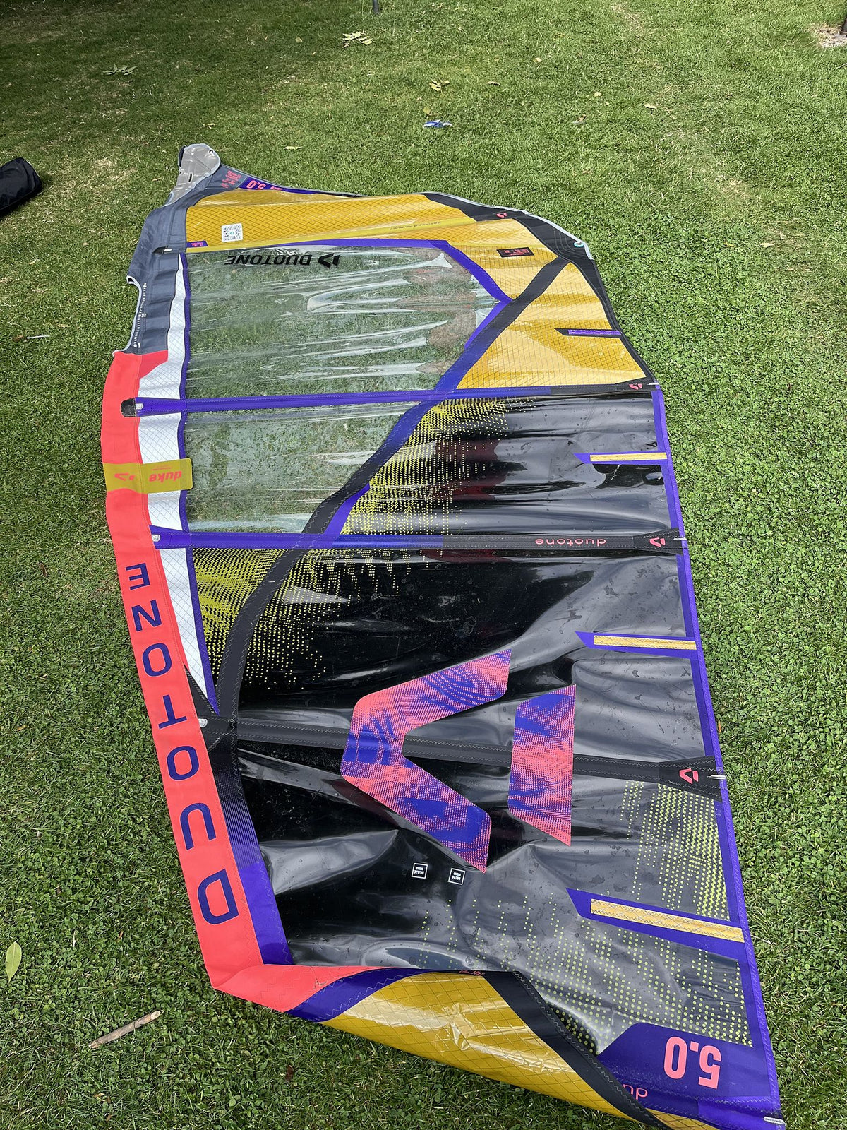 Duotone Duke 5 2026 Kiteboard gelb blau rot mit Finnen, Draufsicht auf Rasen