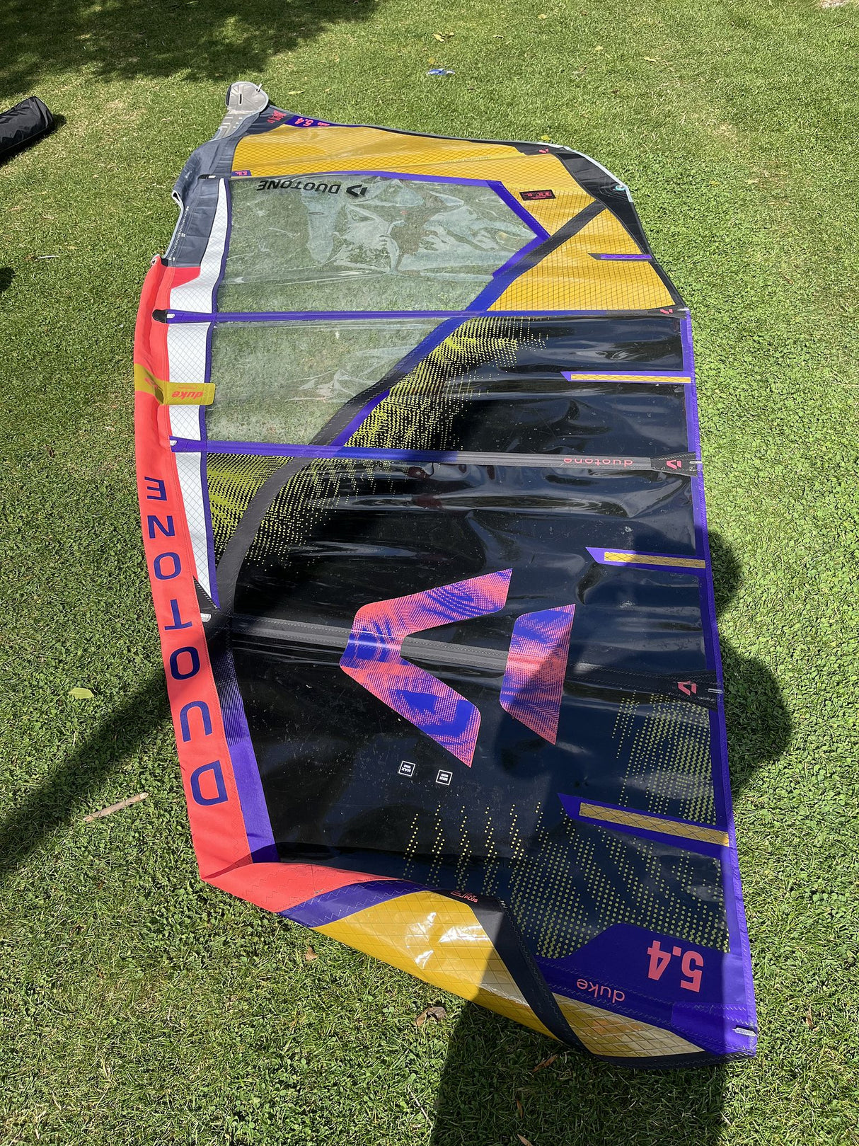 Duotone Duke 5.4 2026 Kiteboard in Gelb, Blau und Rot, aufgelegt auf Rasen, Draufsicht